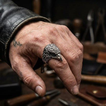 Sterling silver eagle head ring worn on man's index finger with leather jacket in workshop setting