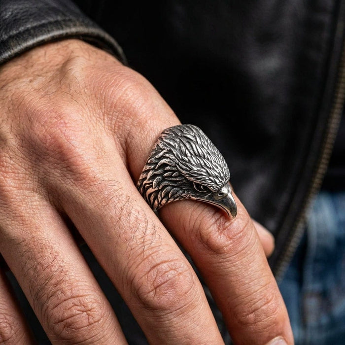 Close-up of handcrafted eagle head ring on man's finger showing intricate feather carving and piercing eye detail