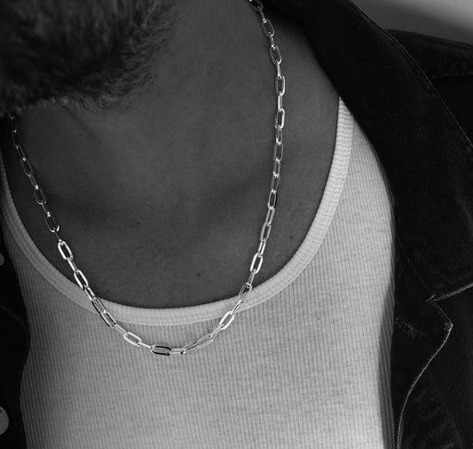 Kille som bär ett halsband med en silverkedja med ovala länkar.