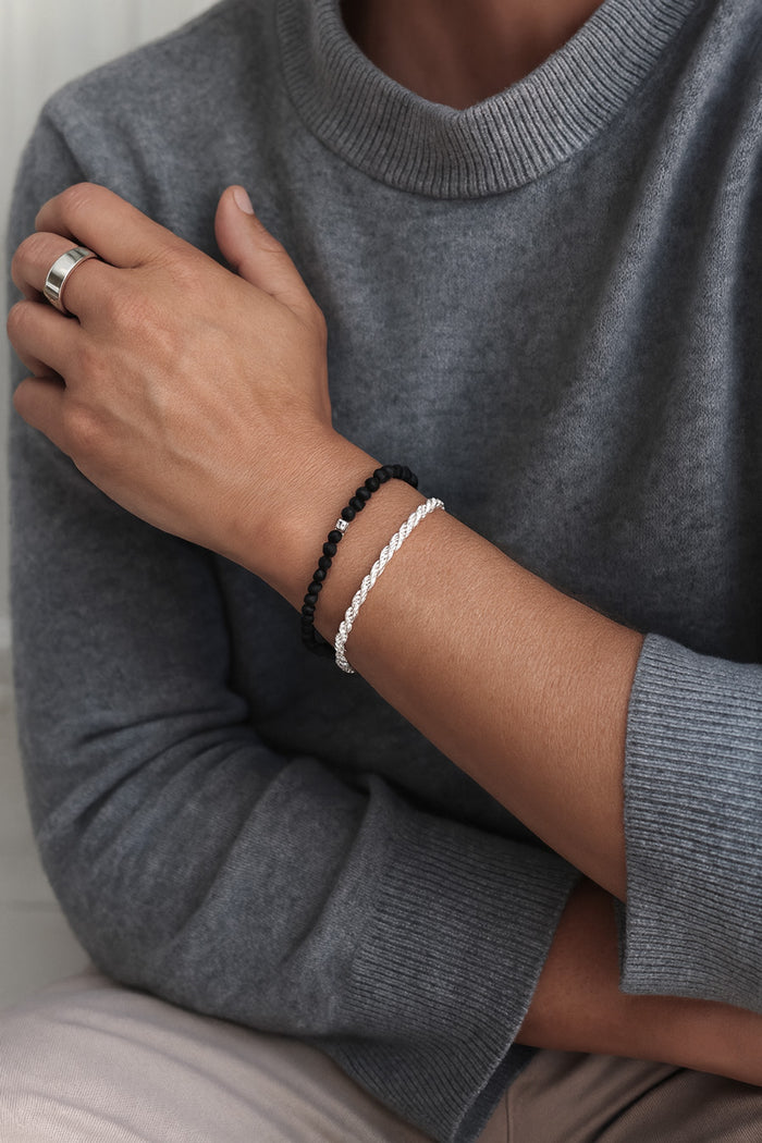 Man som bär ett silverarmband med vriden kedja - Rope Chain / Cordell kedja i silver. Kombinerat med svart stenarmband.