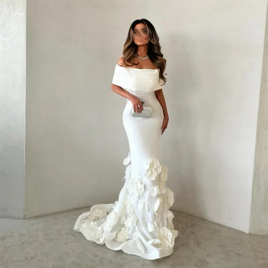 Woman wearing a white off-shoulder gown with floral details against a plain background
