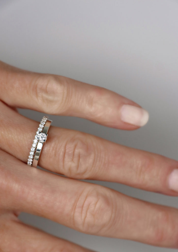 Kvinna som bär set med vigsel och förlovningsringar i silver. Alliansring + solitärring med vita gnistrande diamanter.