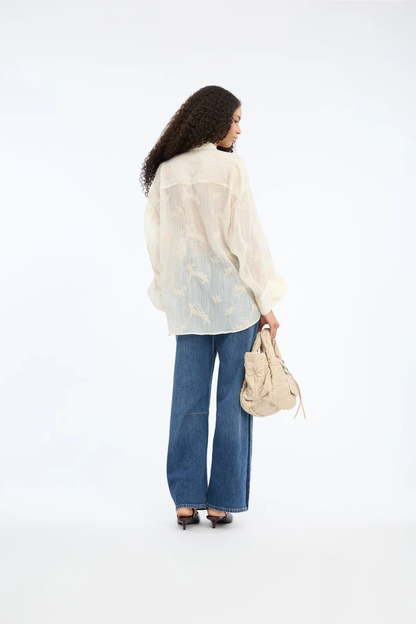 Model wearing the MUNTHE Fortunato Top Crème with textured detailing, loose fit, paired with wide-leg jeans, shop Munthe at Dotique.