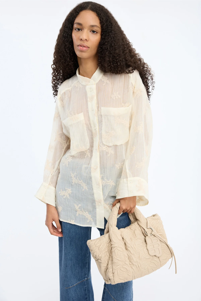 Woman wearing the MUNTHE Fortunato Top Crème with floral embroidery and relaxed fit, styled with blue jeans and a beige textured bag, shop Munthe at Dotique.