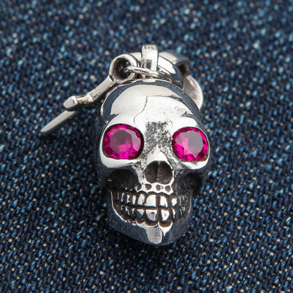 A front view of the sterling silver number 13 skull charm pendant with a dangling cross and red eyes.