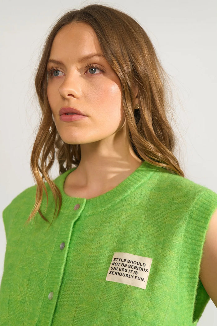 Close-up of a model wearing Numph 706928 NURIETTE CHECK VEST – Jasmine Green with front snap buttons and textured check pattern by Numph. Shop Numph at Dotique.