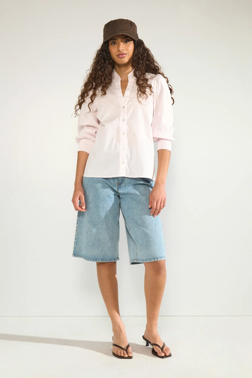 Model wearing Numph 707070 Nulili Blouse Pink Lady with subtle stripes and button front, paired with denim shorts by Numph. Shop Numph at Dotique.