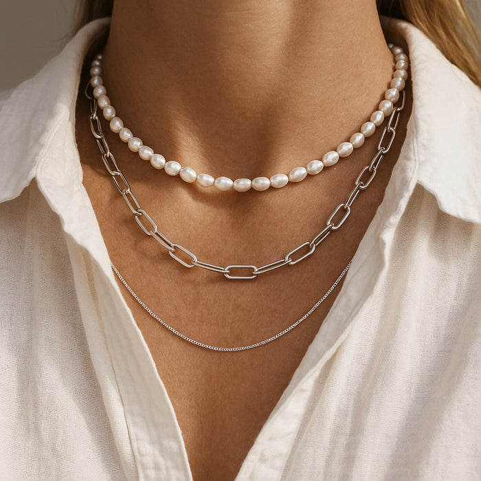 tjej som bär flera halsband i olika längder. Ett pärlhalsband, ett halsband med kedja och en tunn silverkedja.