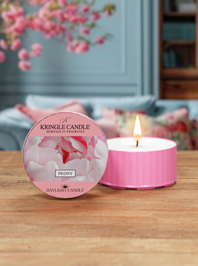 Pink Kringle Candle with floral design on a wooden surface, with a blurred indoor background.