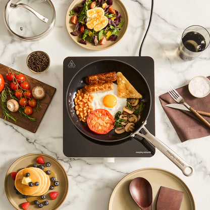 single induction hob with frying pan on top filled with full english breakfast ingredients