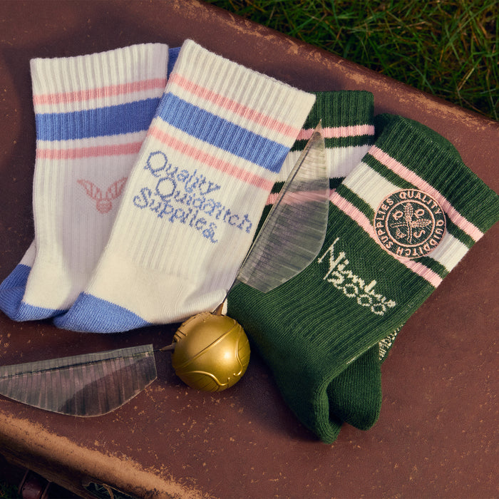 Two pairs of Quidditch socks with branding on a rustic surface with a golden snitch.