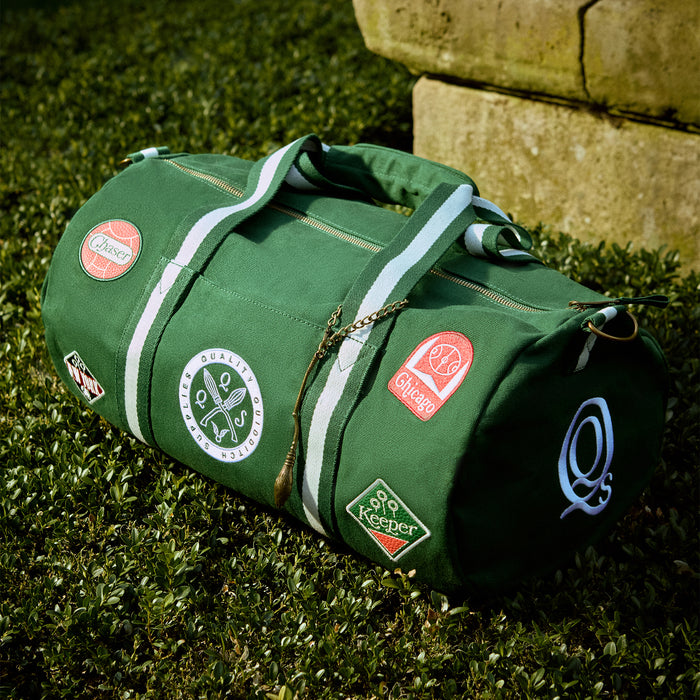Green duffel bag with various Quidditch  patches on a grassy surface