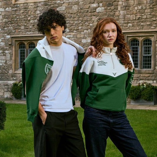 Two people wearing green and white Quidditch 3/4 zip sweatshirts with logos in front of a stone building.