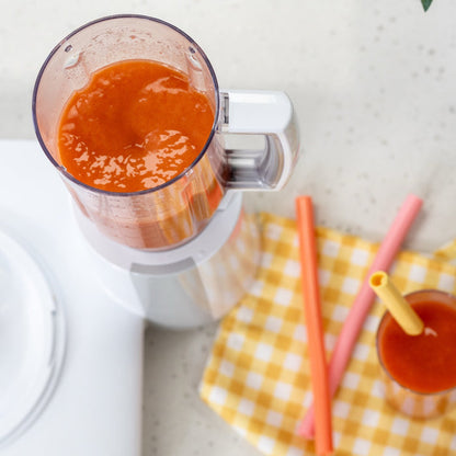 Bosch blender attachment filled with a red drink on a yellow checkered cloth with straws, all on a white counter