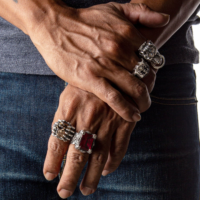A fantasy ring for men with a large ruby-red CZ, shown as part of a collection on a man's hands with other biker rings.