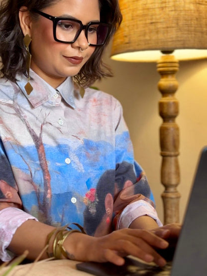 Woman wearing the Shakuntala shirt, working at a laptop, seen from the front with sleeves rolled up