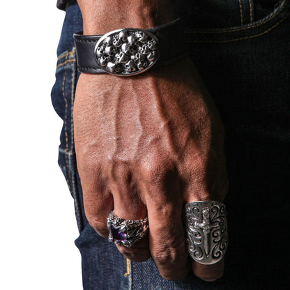 A man's wrist wearing the heavy 65-gram sterling silver skull leather bracelet, paired with biker rings.