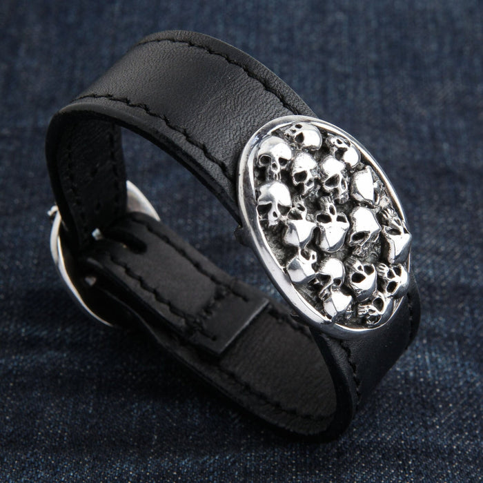 A detailed close-up of the pile of skulls design on the solid silver plate of the leather bracelet.