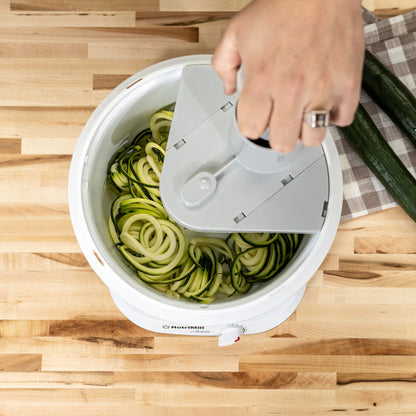 A man using a NutriMill spiralizer attached to a NutriMill artiste mixer on a wooden counter