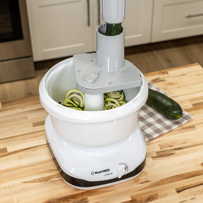 A NutriMill artiste mixer cutting zucchini with the spiralizer attachment on a wooden counter