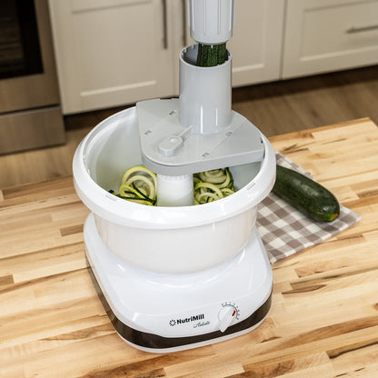 A NutriMill artiste mixer cutting zucchini with the spiralizer attachment on a wooden counter