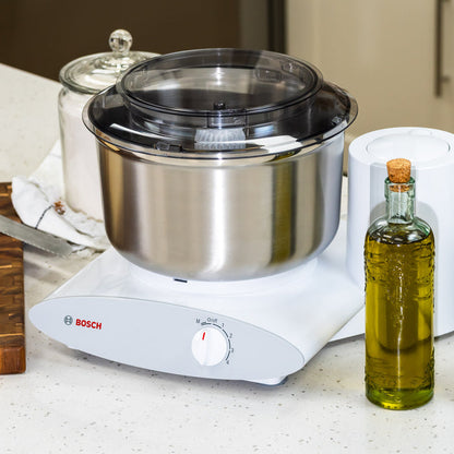 Bosch White Universal Plus Mixer with stainless steel bowl on white counter next to oil.