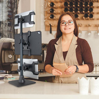 A woman in glasses and an apron stands behind a counter with paper bags. Next to her is the Triple Slim-Grip® Tablet Holder Stand for Restaurant Delivery and Point of Sale—ideal for DoorDash, Uber Eats, or Grubhub. Coffee shop equipment is seen in the background.