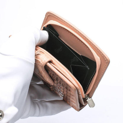 Gloved hand opening zippered coin pocket of old rose crocodile wallet revealing dark green fabric lining and silver zipper pull