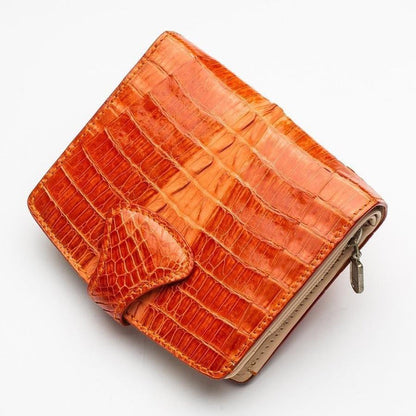 Diagonal view of the triangular snap tab closure with fine crocodile scale texture on the orange exotic leather wallet