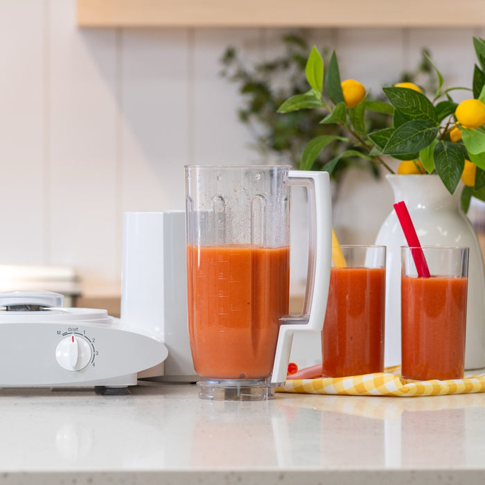 Bosch blender attachment with a red drink inside on a white kitchen counter next to glasses filled with the same juice