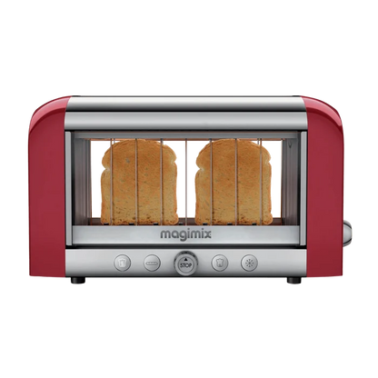 A red Magimix toaster with transparent glass side windows showing toasting bread, featuring stainless steel and borosilicate glass construction with control buttons on the front.