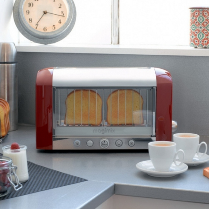 A red magimix red vision toaster toasting bread on a grey background next to cups of tea