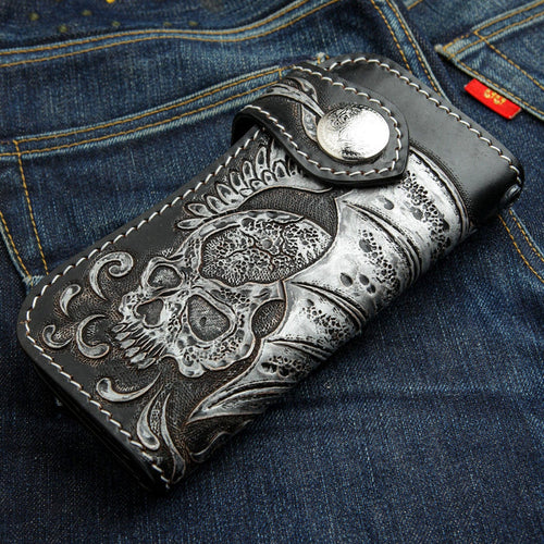 The winged skull biker wallet shown folded and resting on a pair of denim jeans.